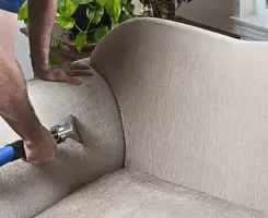 Professional upholstery cleaner deep-cleaning a fabric sofa with a handheld extraction tool and hose in Madison, WI.